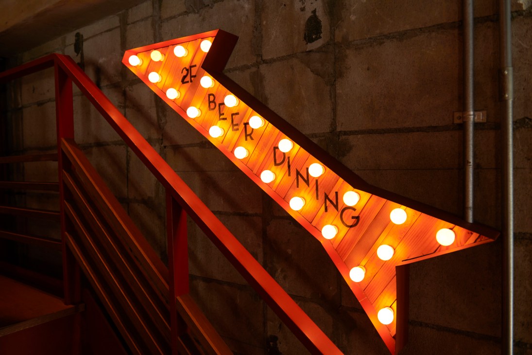 Illuminated orange arrow sign with light bulbs spelling 'BEER DINING' pointing toward restaurant entrance