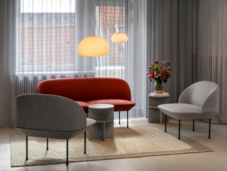 A Scandinavian-style sitting area with a rust-red sofa, grey armchairs, round pendant lights, and sheer curtains.
