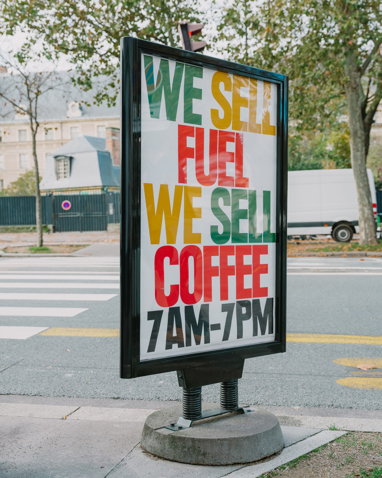A black-framed sidewalk sign advertising fuel and coffee with colorful text reading WE SELL FUEL WE SELL COFFEE 7AM-7PM