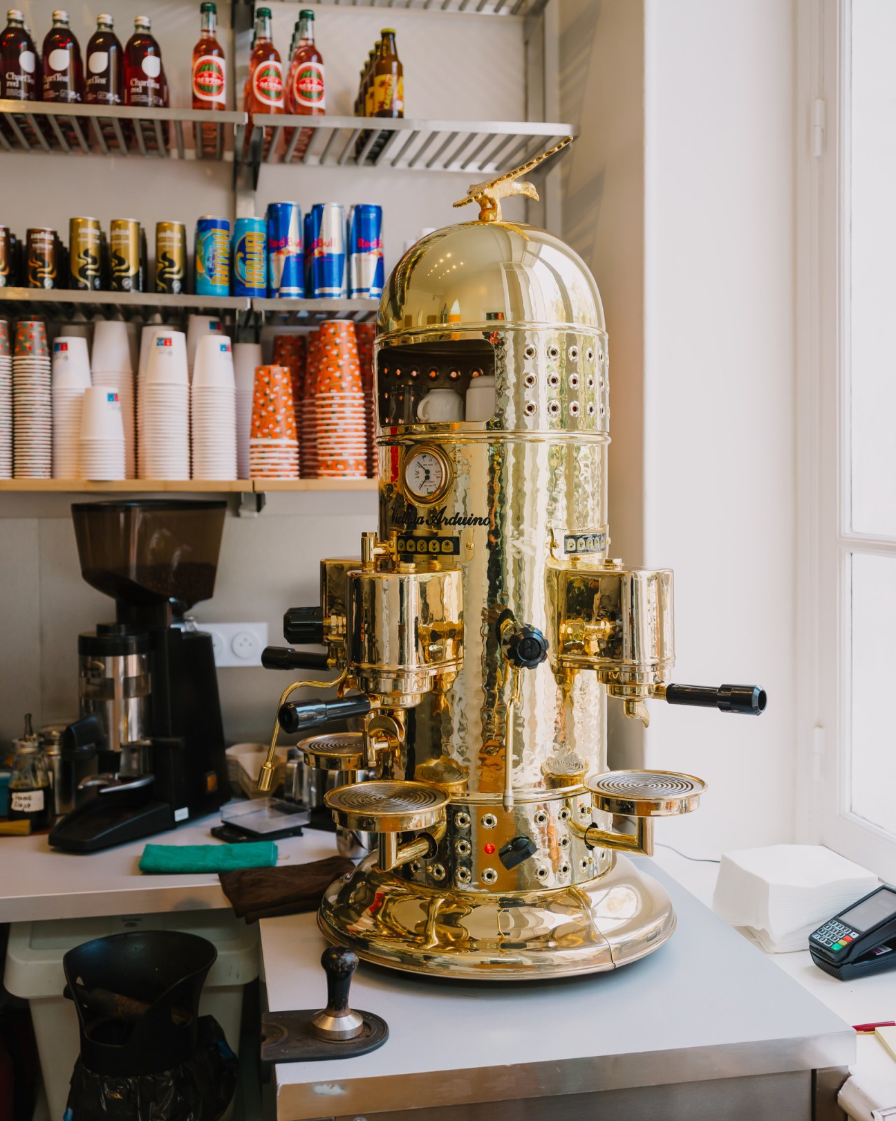 Ornate golden brass espresso machine with multiple portafilters on white counter in commercial kitchen setting