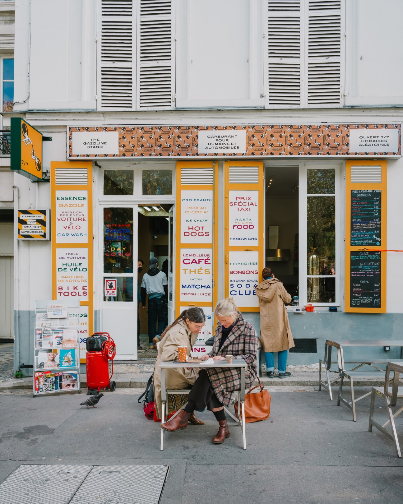 Two elderly women sit at a small table outside The Gazoline Stand service station in Paris