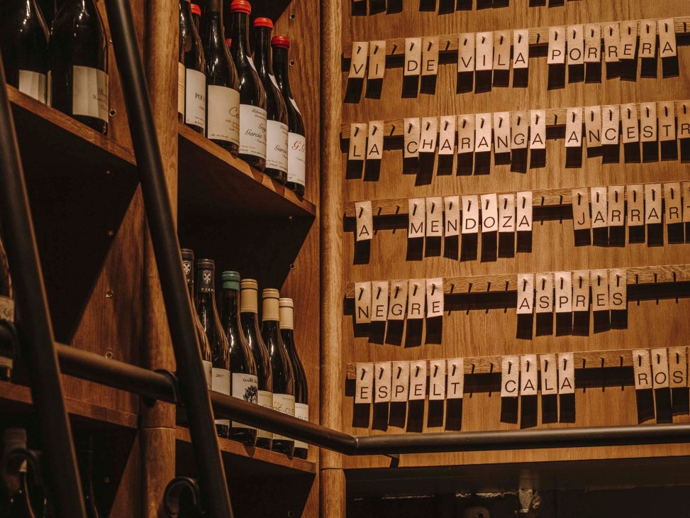 Wine storage system with wooden compartments labeled with Spanish wine region names like Vila Porrera, Charanga Ancestr