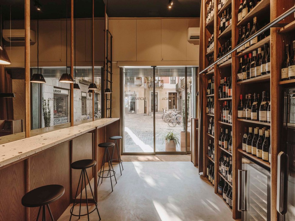 Interior of Normal restaurant with wooden wine shelving, bar seating, and view to street through large windows