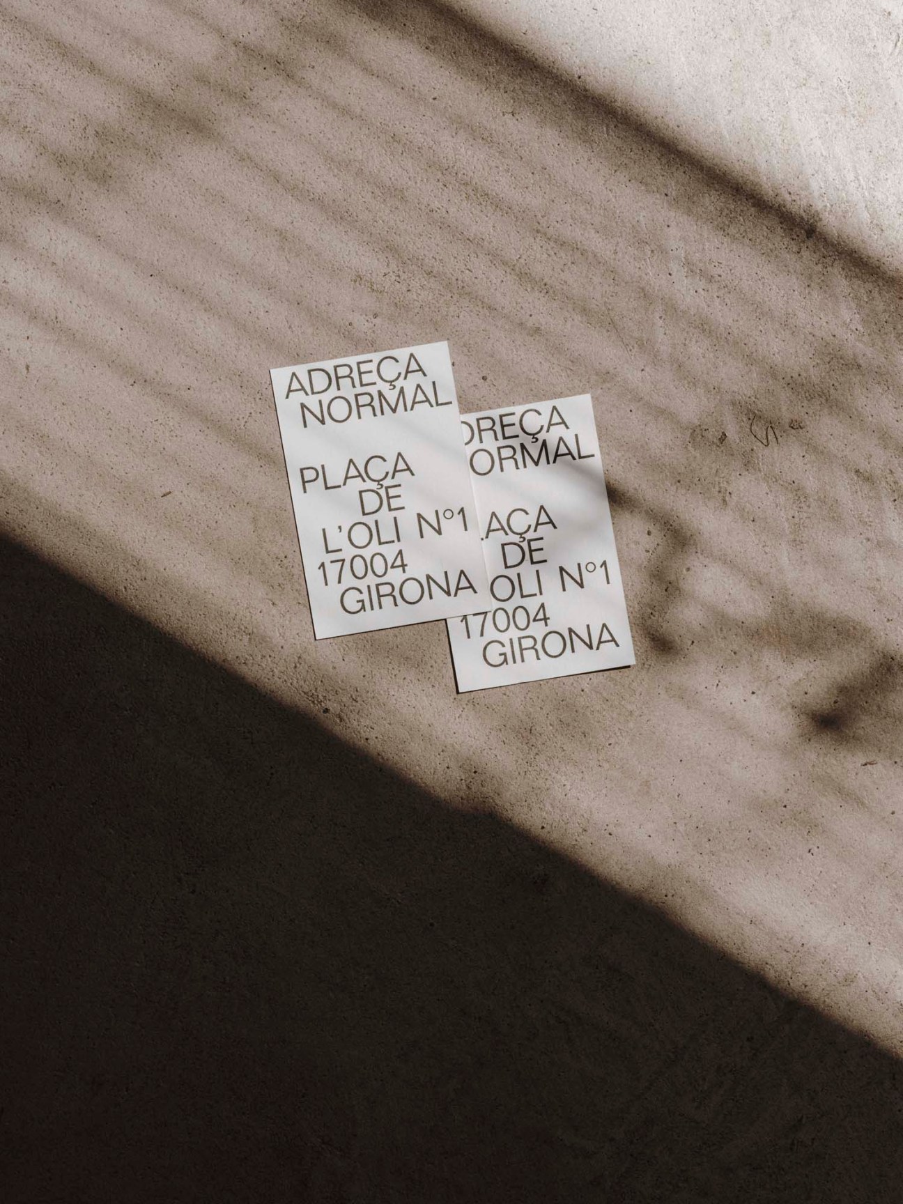 Two white business cards with Normal restaurant branding lying on rippled sand with shadows