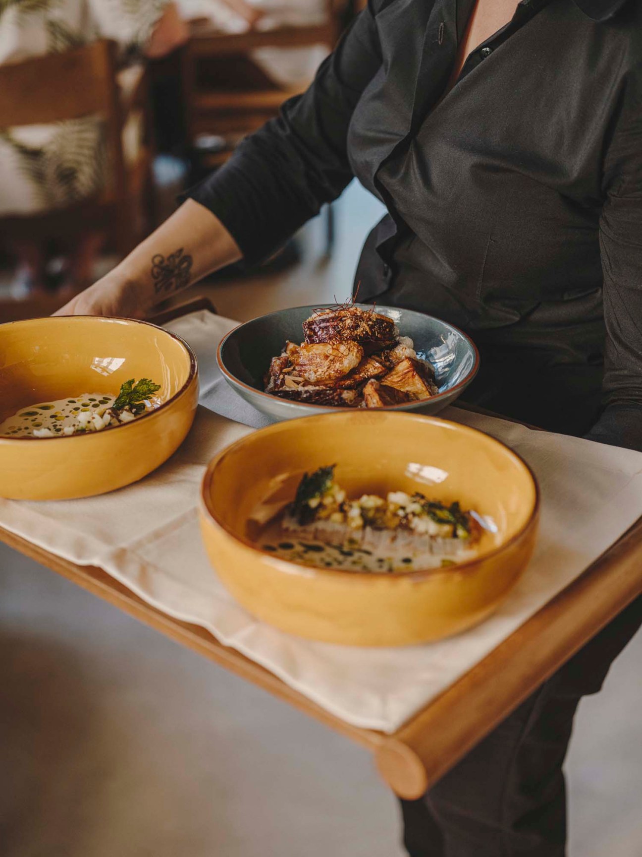 Three dishes arranged on a wooden tray - two yellow ceramic bowls and one dark bowl containing prepared food at Normal restaurant