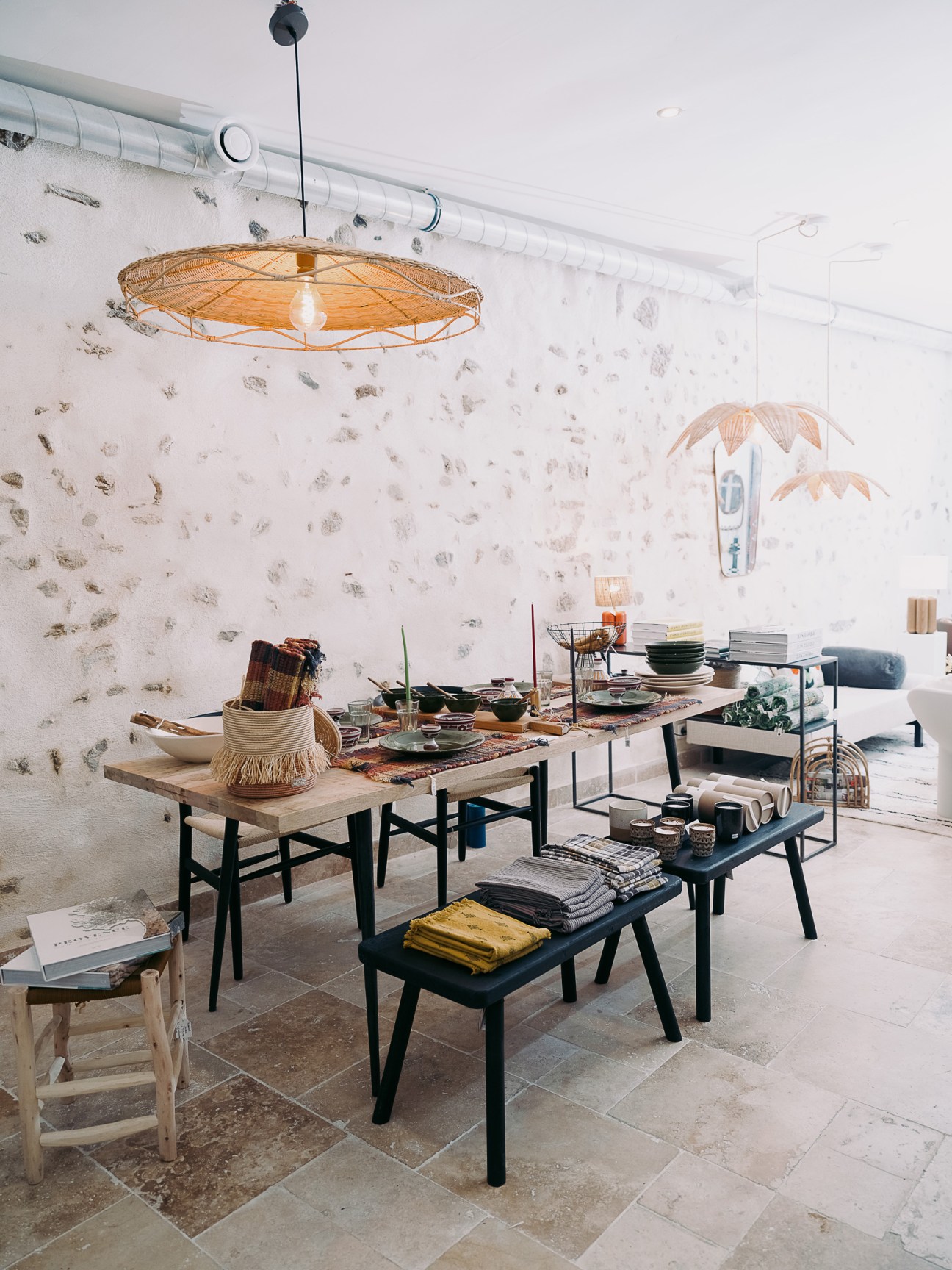 Modern retail space with woven pendant lamp, white speckled wall, and wooden display tables with ceramics and homeware.