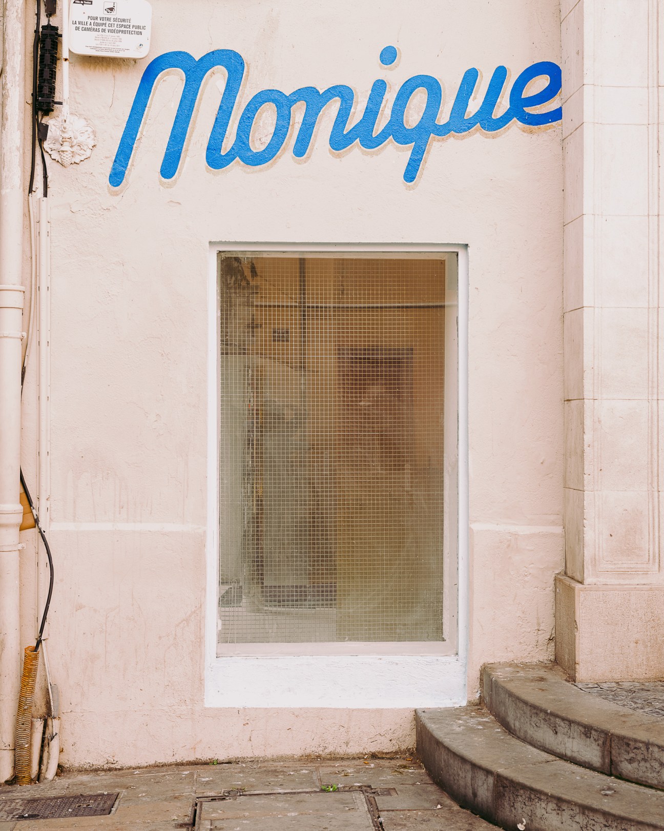 Storefront with blue neon 'Monique' sign on pale pink building in Toulon, France.