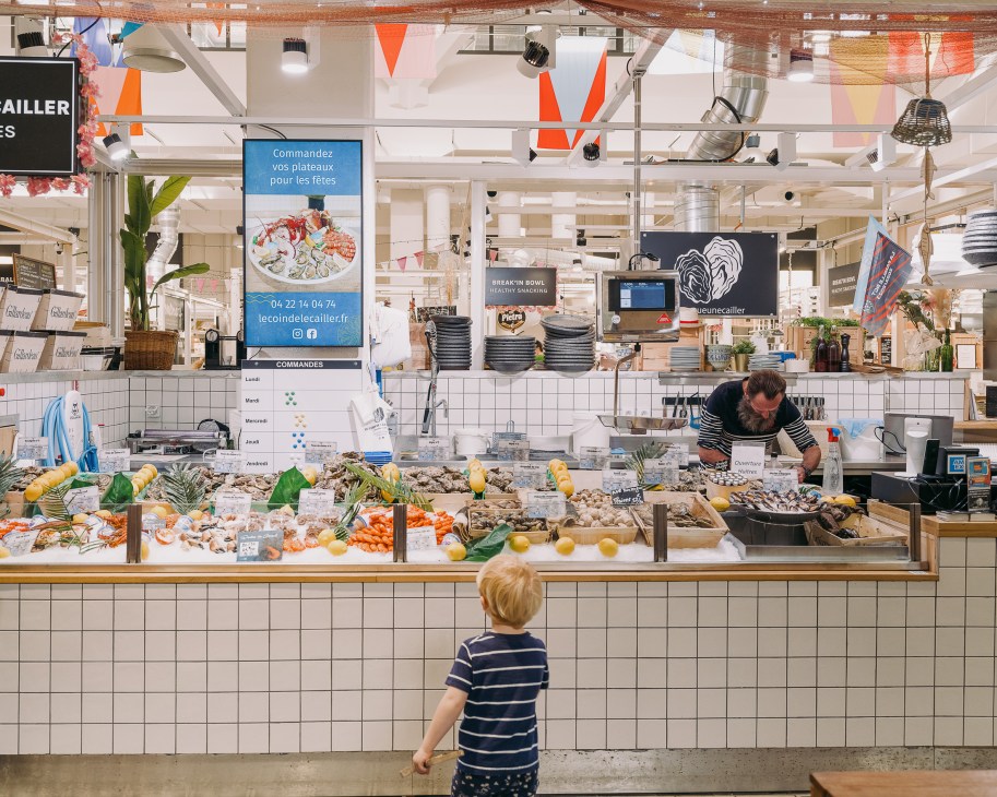 Child viewing a seafood market stall display with fish, shellfish and lemons at a covered market in Toulon.