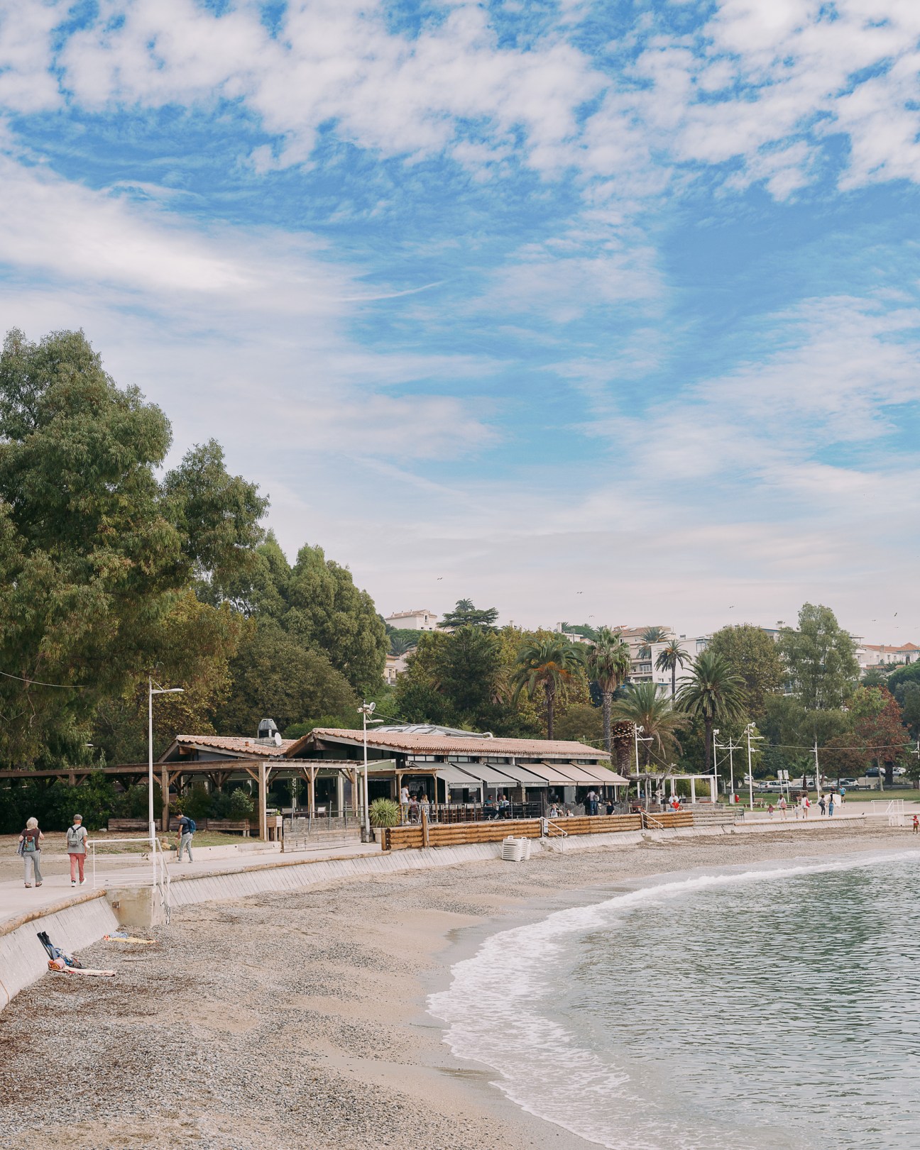Beach promenade with wooden structures and palm trees overlooking Mediterranean waters.