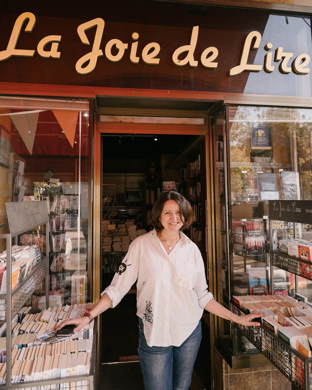 Woman standing in doorway of La Joie de Lire bookstore with displays of books visible in windows