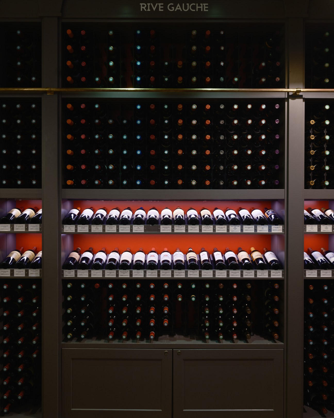 Wine bottles displayed in a modern cellar storage system with organized rows and 'RIVE GAUCHE' sign above