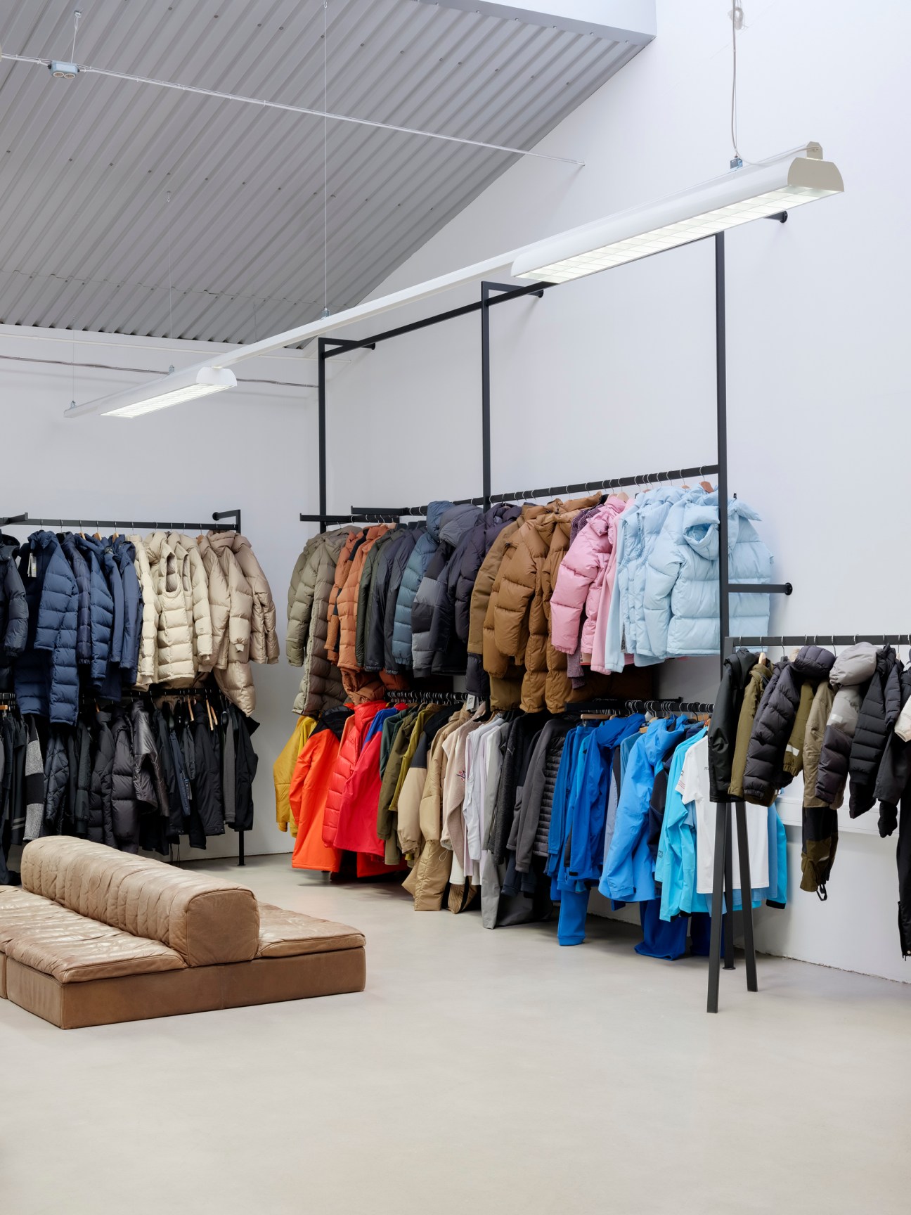 66°North showroom displaying colorful puffer jackets and outerwear on black metal rails with minimalist concrete and white interior design.