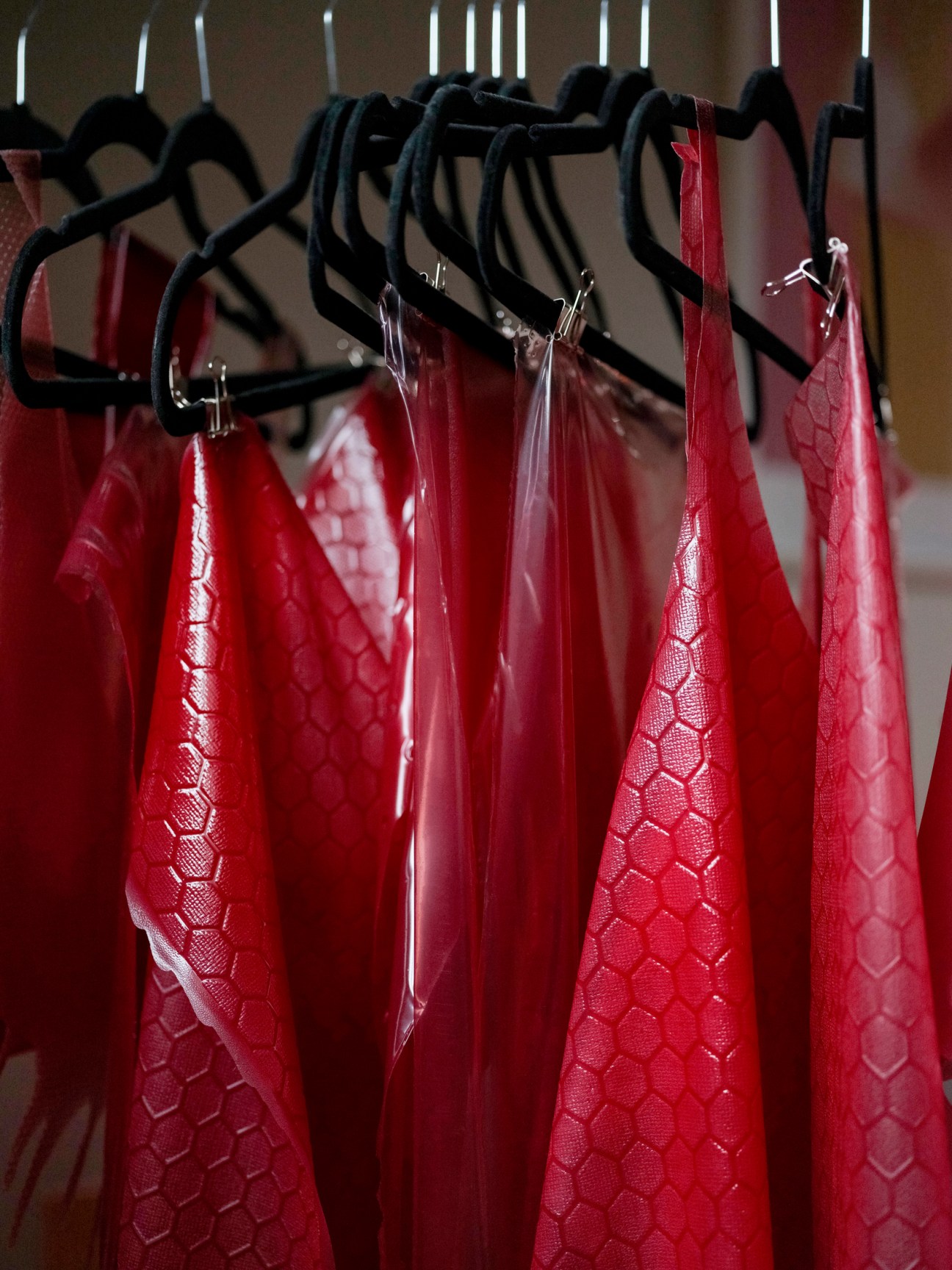 Red gelatin-based fabric samples hanging on black hangers under studio lighting