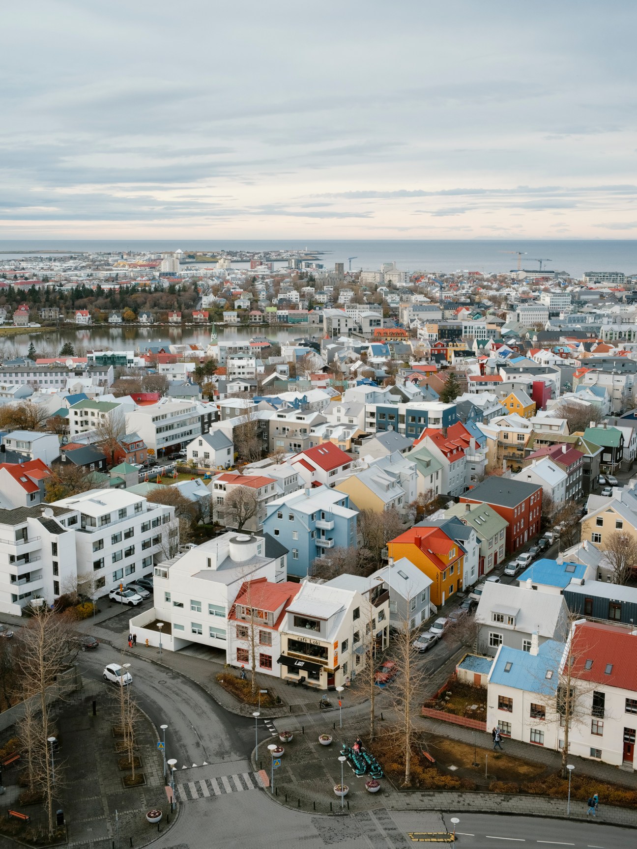Aerial view of downtown Reykjavík showing colorful buildings, a frozen lake, and mountains in the distance under a cloudy sky.