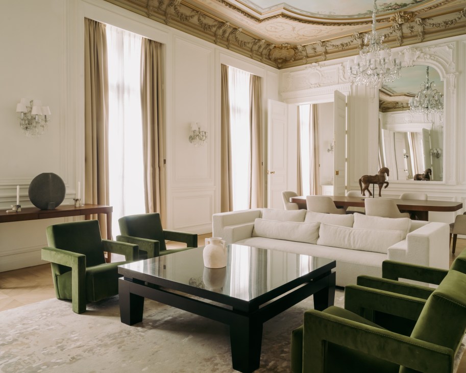 Elegant hotel living room with ornate ceiling, crystal chandelier, green velvet chairs and white sofa