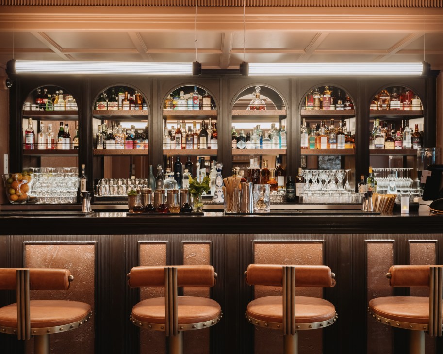 Elegant bar interior with arched shelving displaying bottles, leather bar stools, and black granite counter