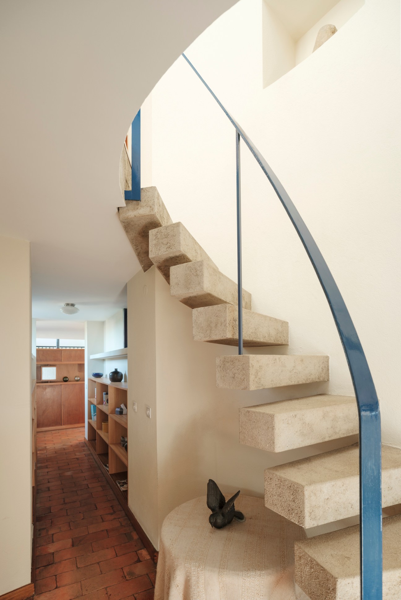 Curved stone staircase with blue handrail spiraling upward in modernist interior