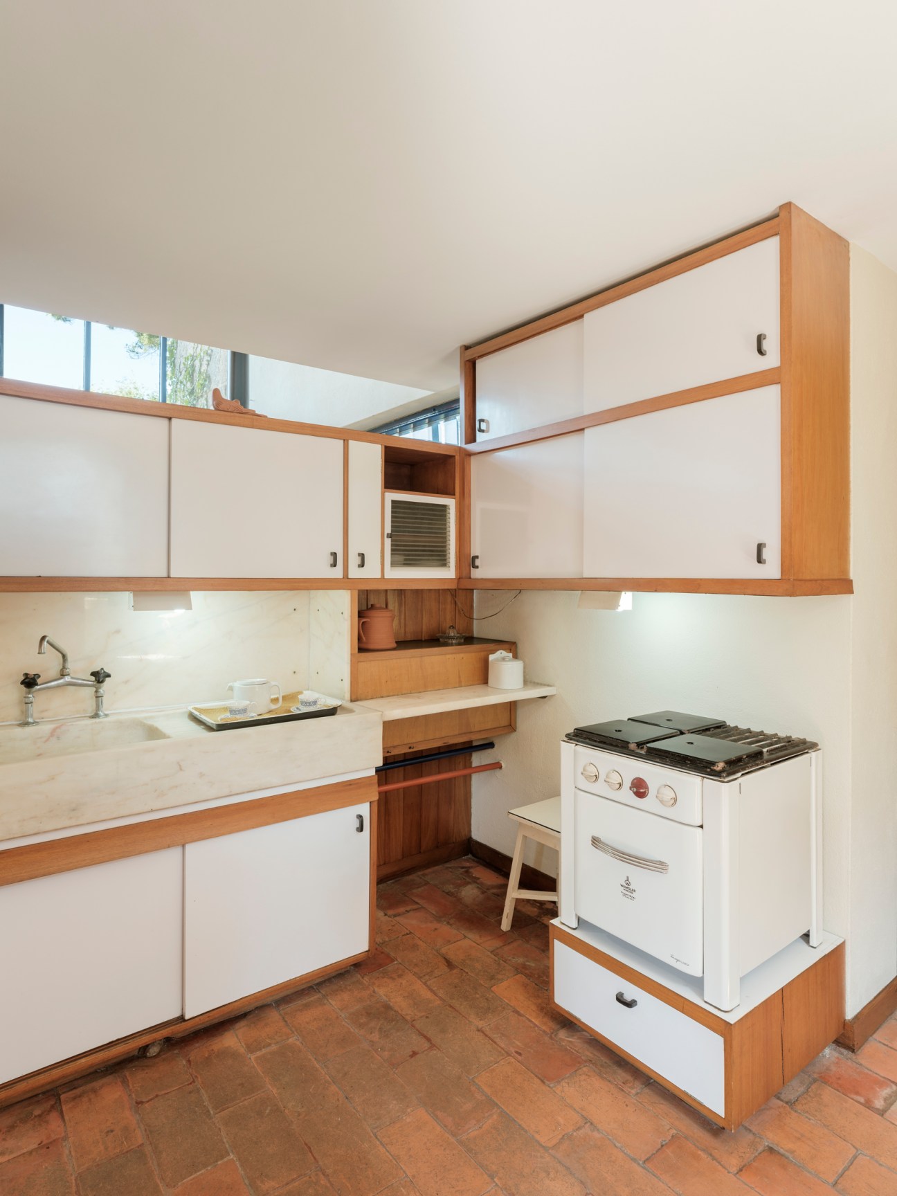 Mid-century kitchen with white cabinets, wood trim, white appliances and terracotta tile floor