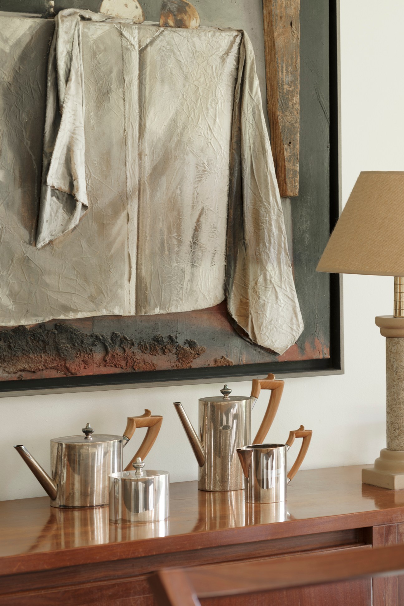 Interior living space with white draped fabric, silver tea service on wooden sideboard, and neutral furnishings