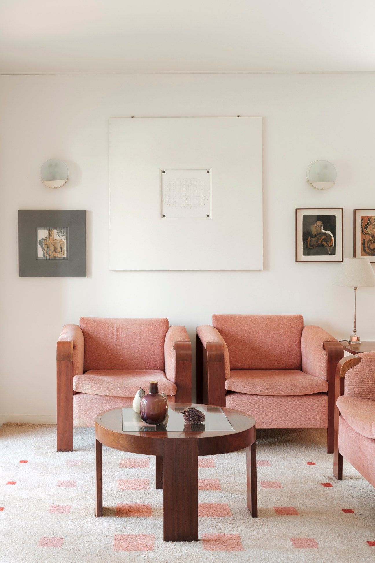 Modern living room with pink upholstered chairs, round glass coffee table, and framed artwork on white walls