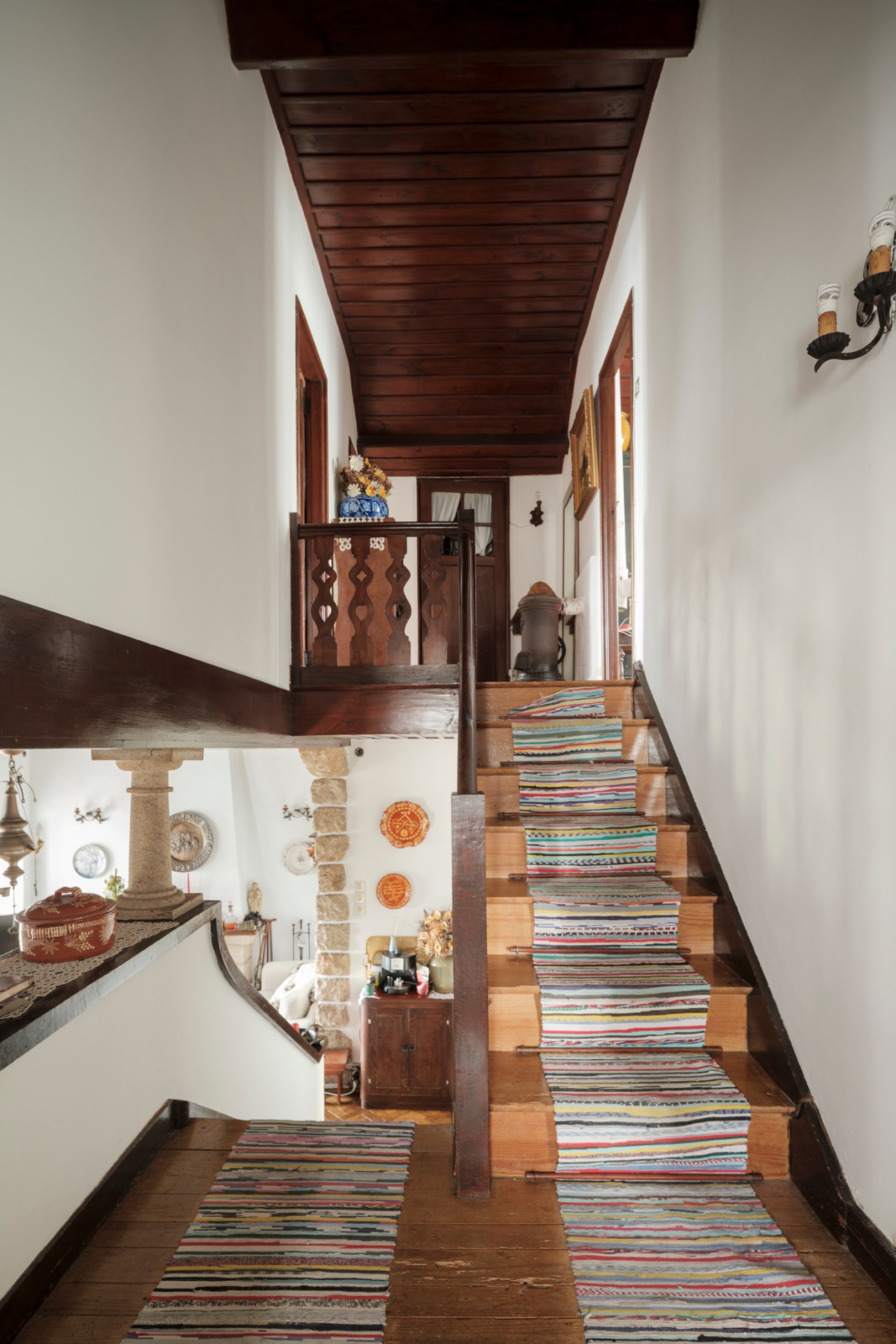 Interior view of wooden staircase with colorful striped runner rugs and exposed ceiling beams