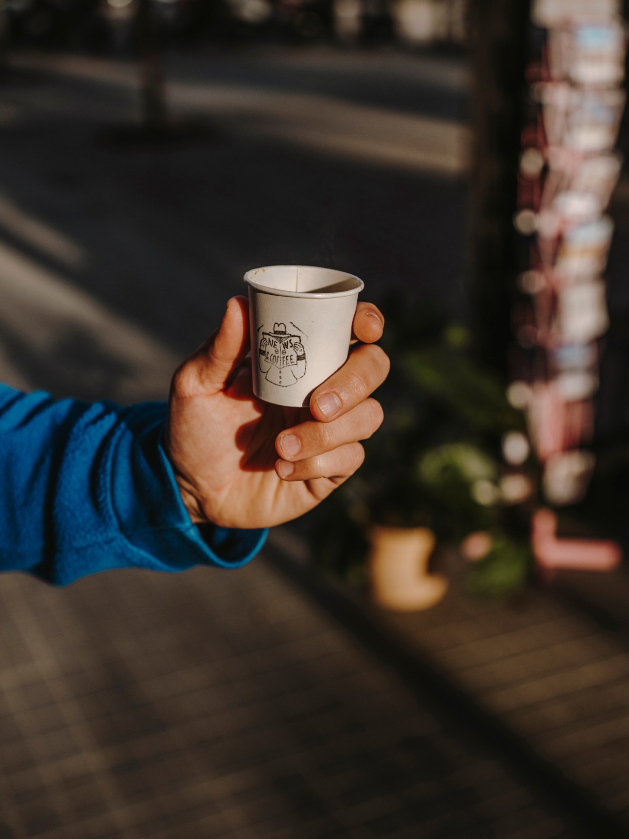 Hand holding white coffee cup with logo outdoors