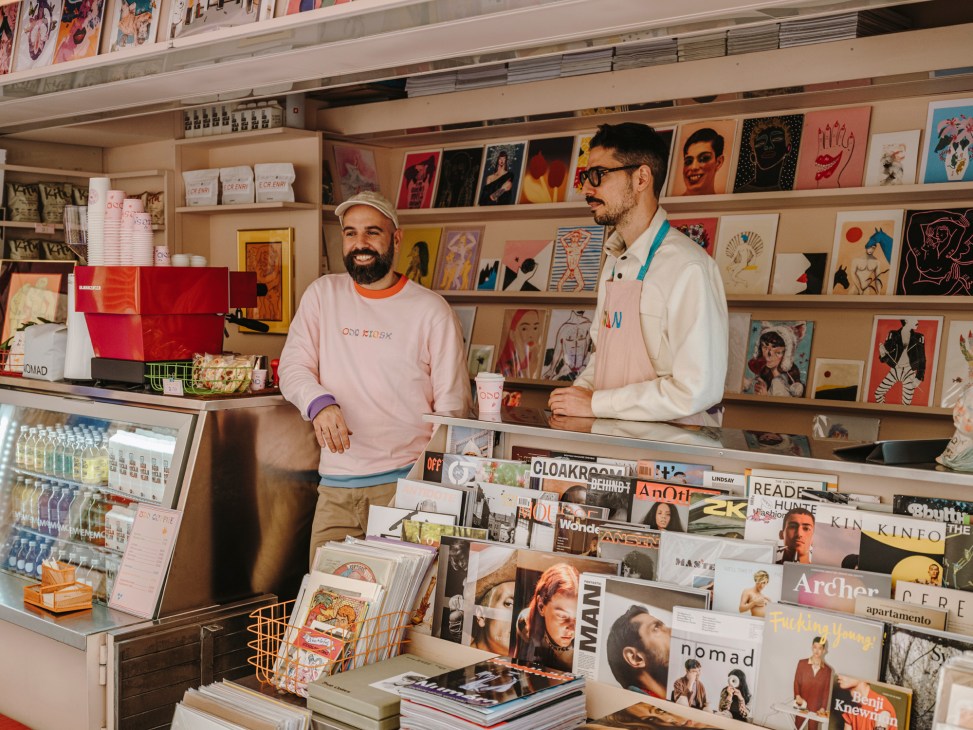 Txema and Ivan from Odd Kiosk standing behind counter surrounded by magazines and colorful publications
