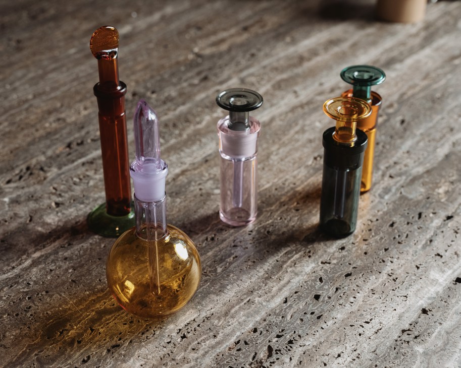 Colorful glass fragrance bottles with various stoppers arranged on concrete surface.
