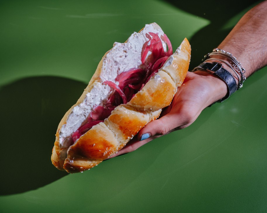Hand holding a challah sandwich with red pickled vegetables and orange segments
