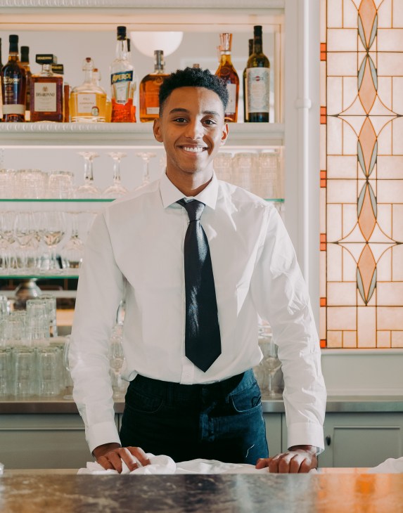 Bartender Jarod Soler smiling behind the bar at Brasserie Emil restaurant.