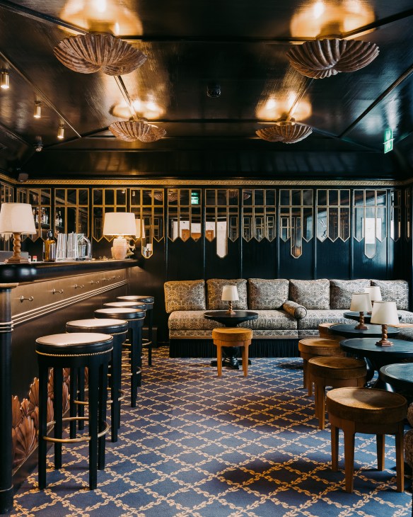 La Coquille d'Or hotel bar with art deco shell-shaped ceiling lamps, dark wood paneling, upholstered seating and brass bar counter.