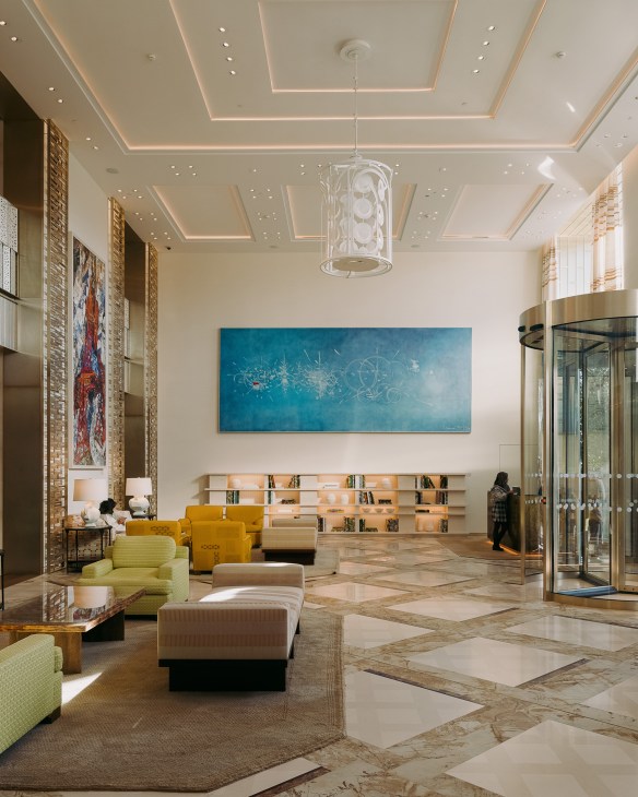 Modern hotel entrance foyer with cream ceiling, yellow chairs, blue artwork, and marble flooring at Le Cheval Blanc Paris.