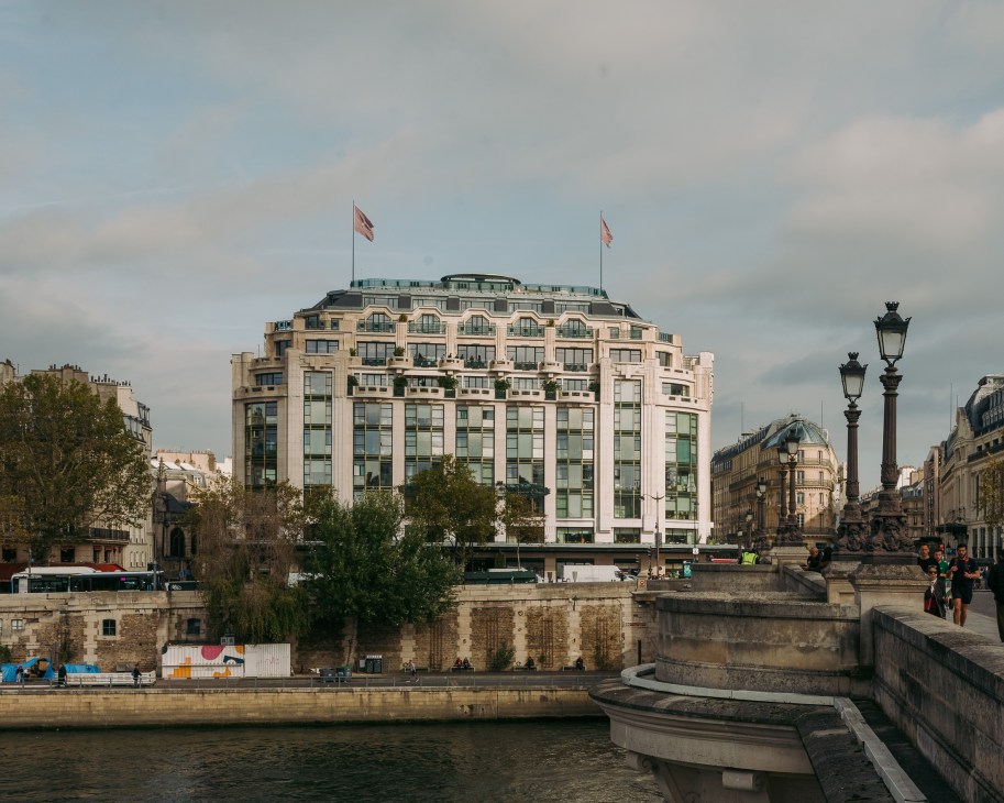 Le Cheval Blanc hotel building on the Seine in Paris with art deco facade and French flags.