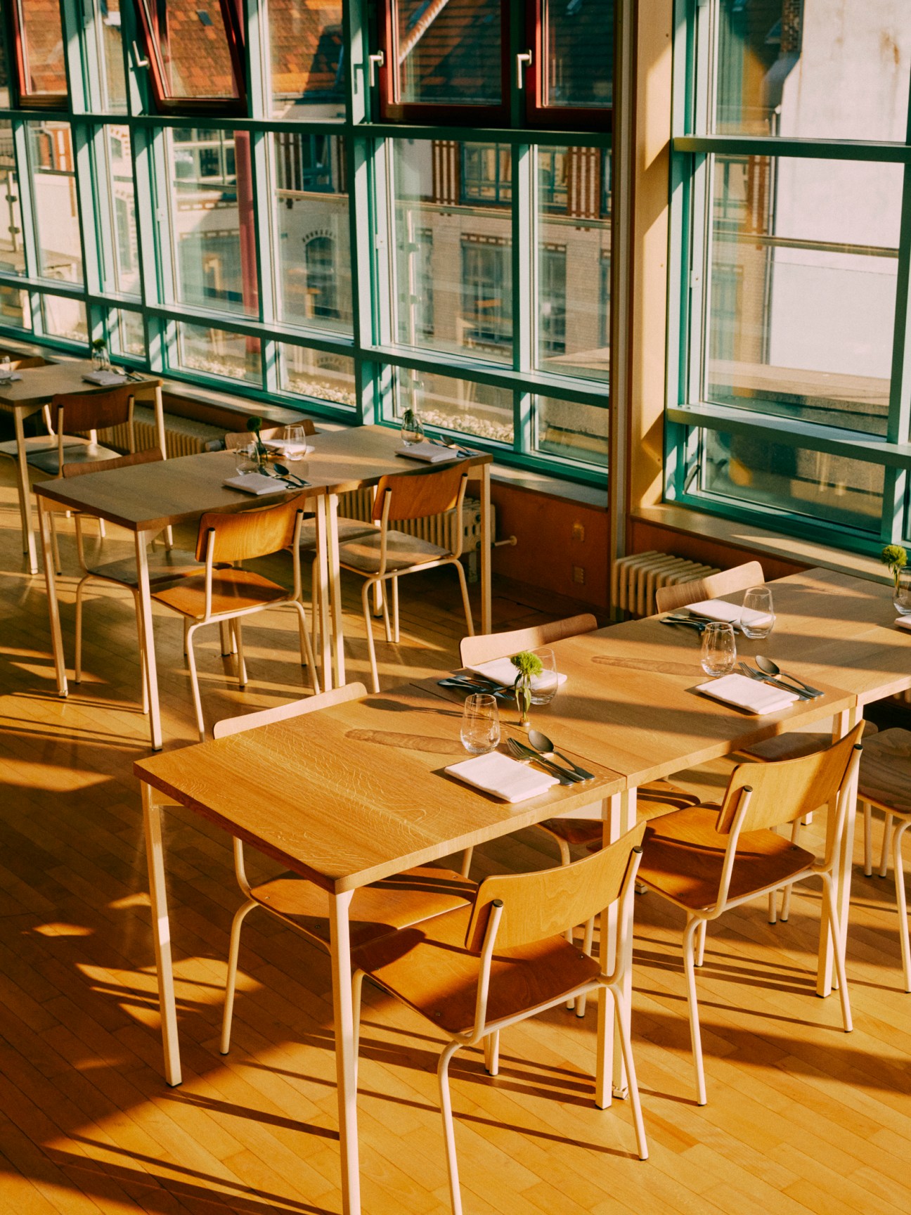 Modern restaurant dining room with wooden tables and chairs bathed in golden sunlight from large windows