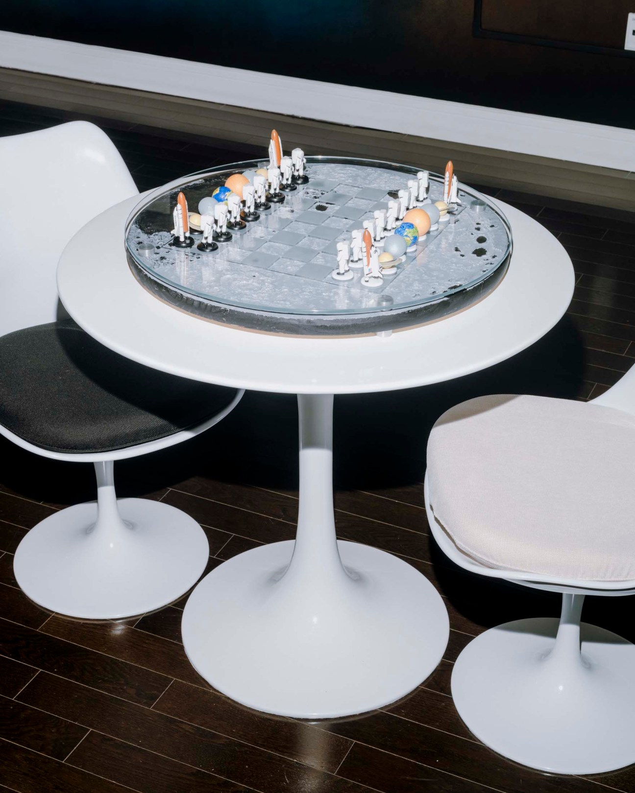 A circular chess board with white base table and black seats, pieces arranged for play.