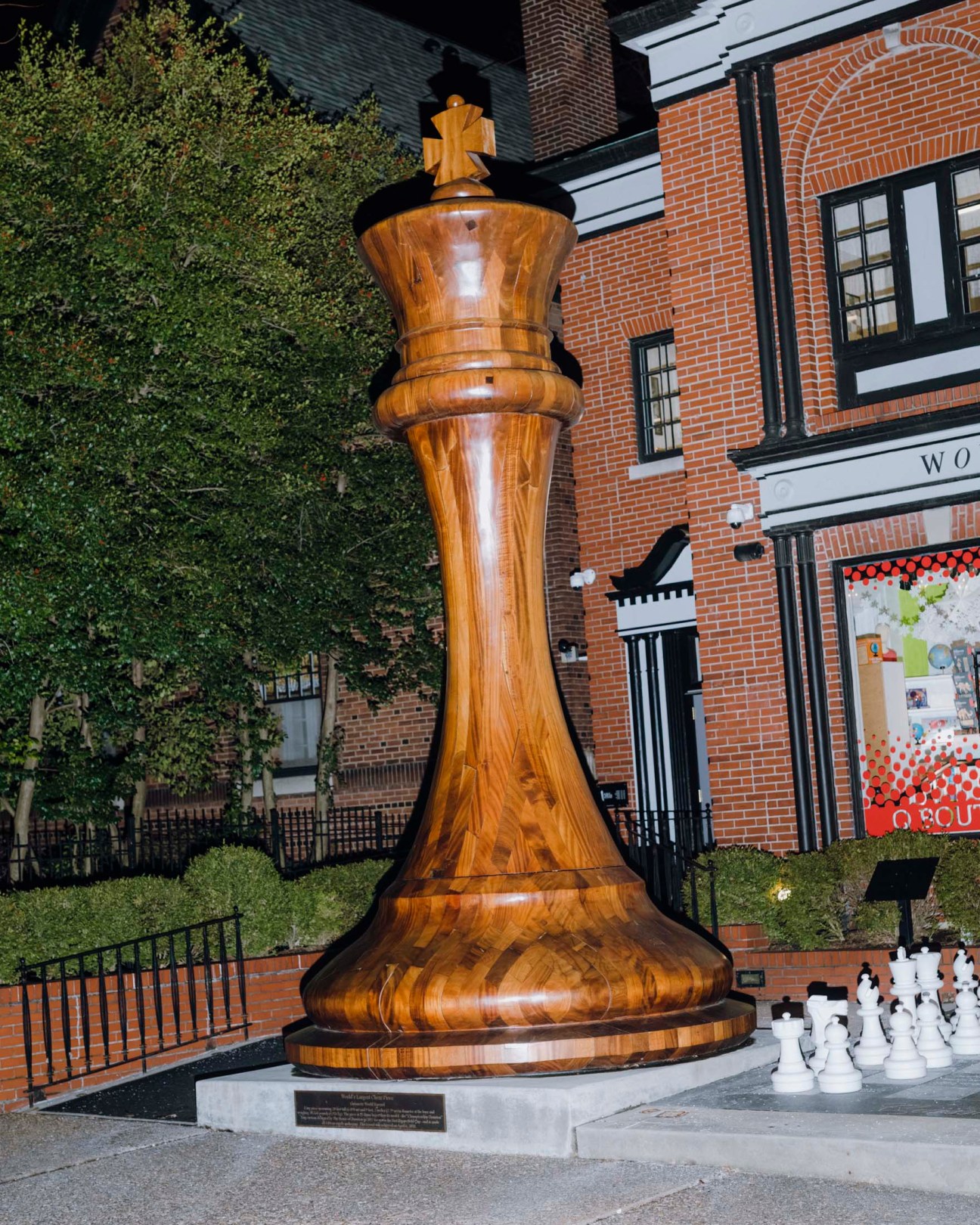 Large wooden chess king piece standing in front of brick building with ivy.