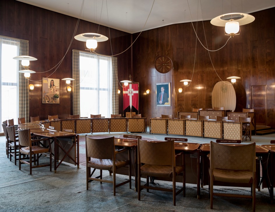 Interior view of Aarhus City Hall council chamber with wooden paneled walls, pendant lights, and rows of seating