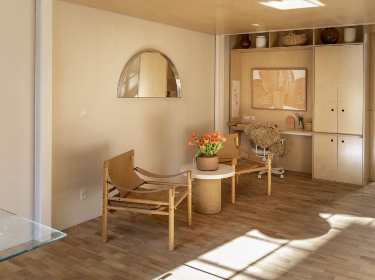 Minimalist interior with wooden furniture, potted flowers, arched mirror and built-in storage cabinetry in warm neutral tones.
