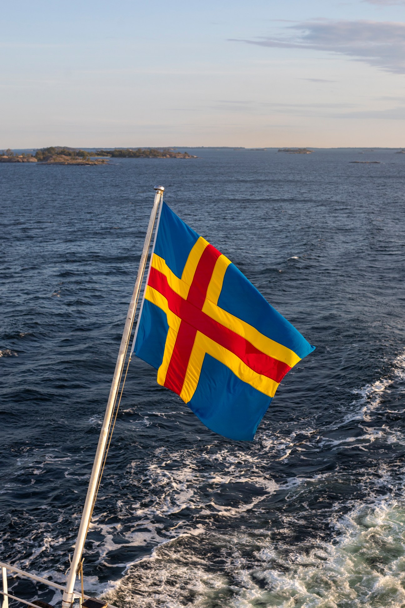 Blue and yellow Åland flag flying on flagpole against water and distant islands
