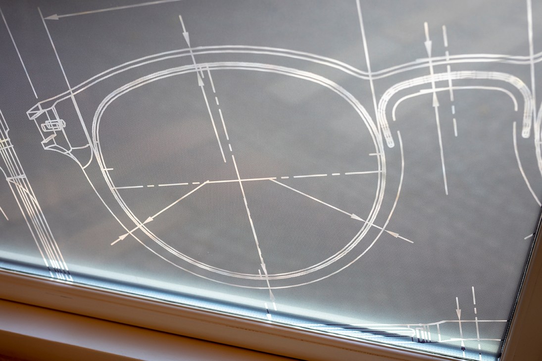 Technical blueprint sketch of eyeglasses showing screwless construction design on a light table.