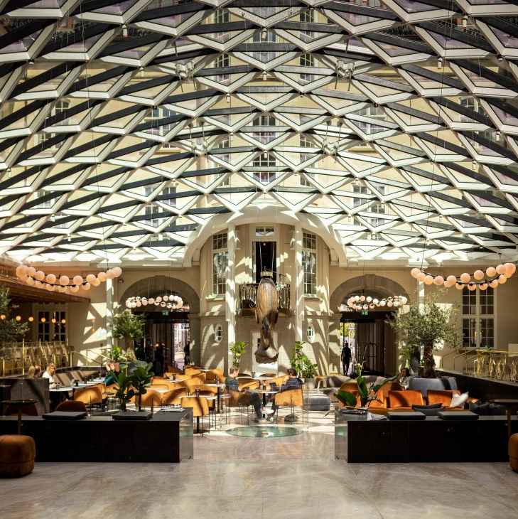 Grand hotel atrium lobby with geometric glass ceiling, cream-colored seating areas, and marble floors