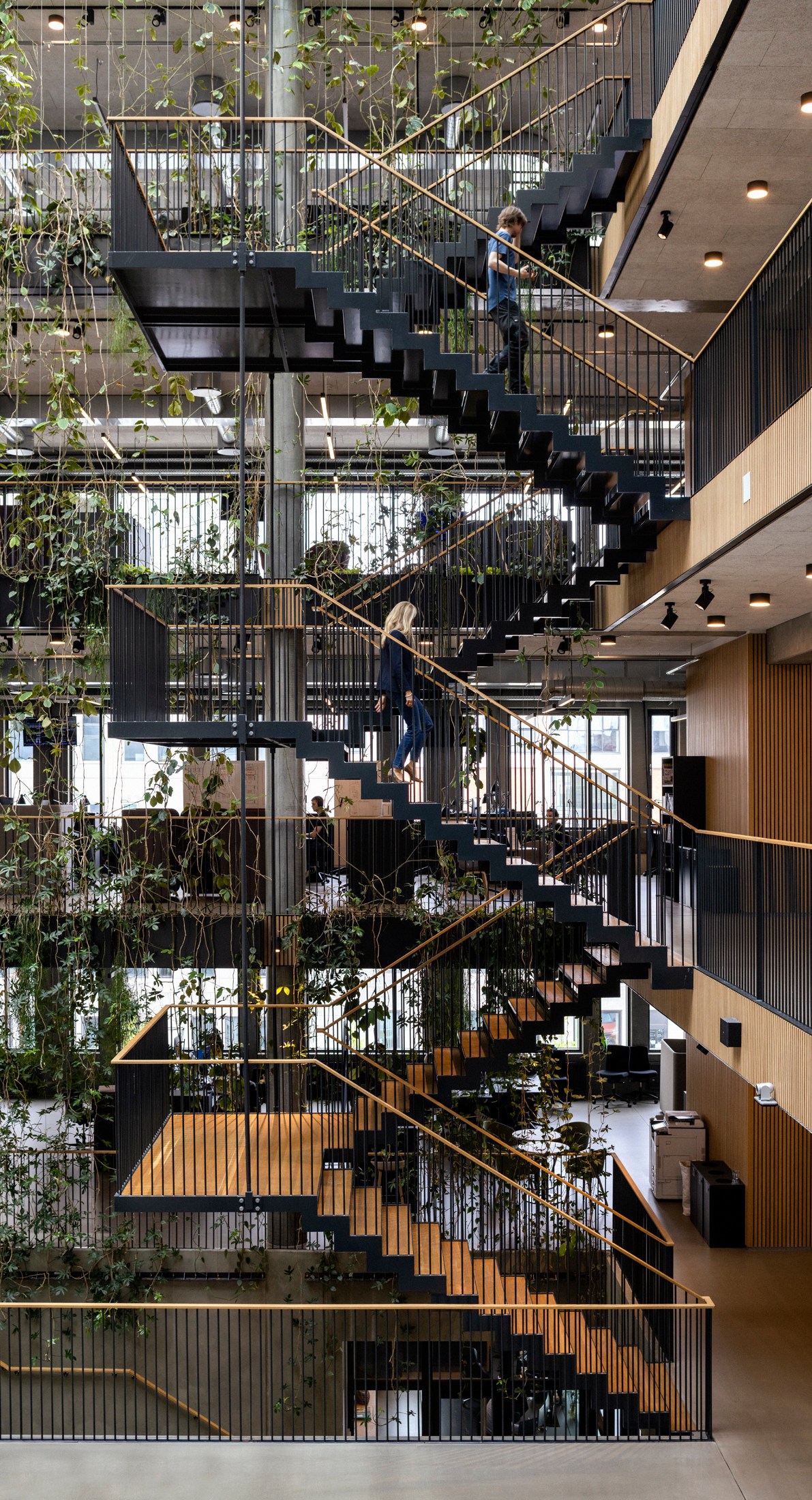 Multi-level modern office interior with black metal stairs, wooden railings, and integrated greenery throughout