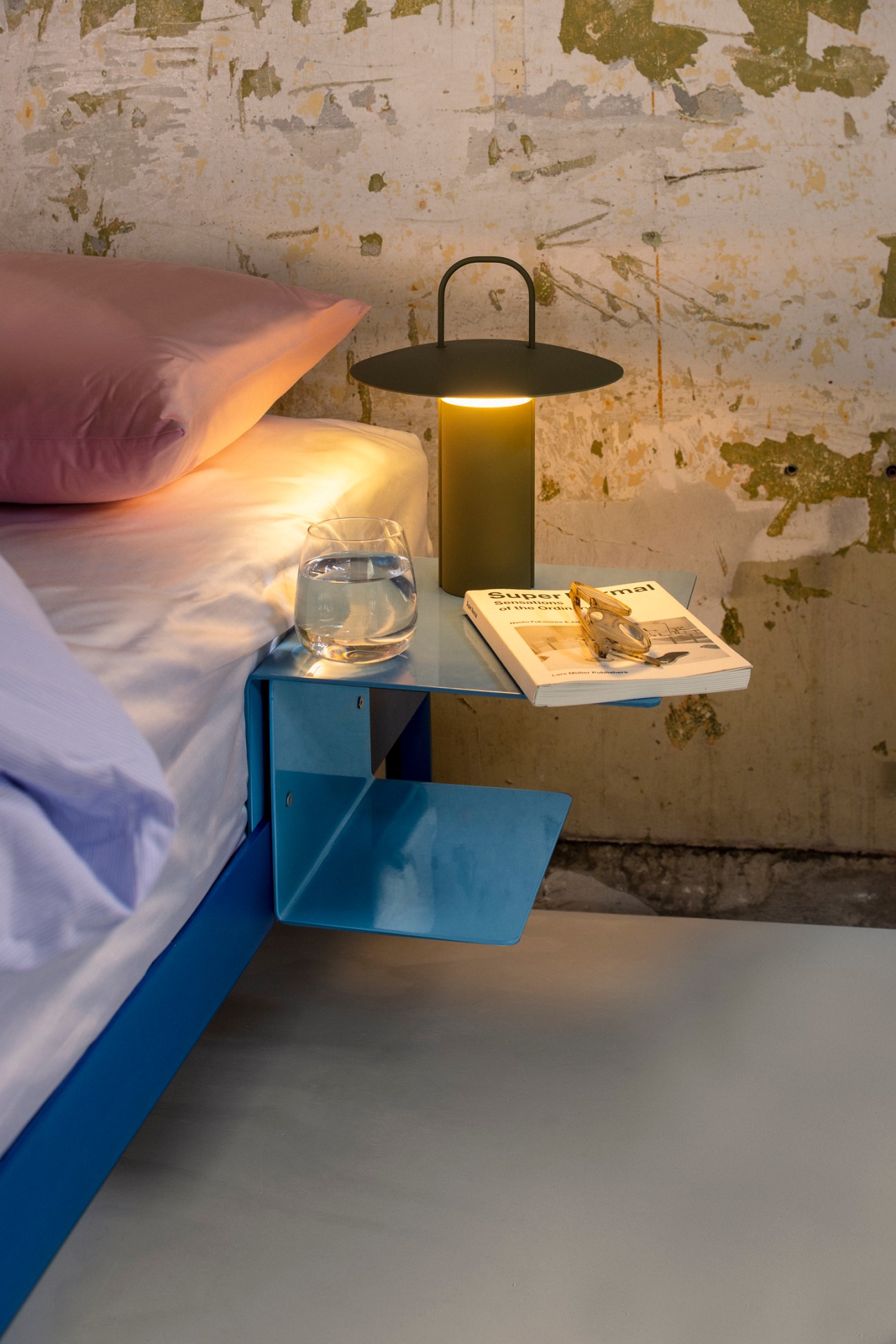 Reframed bed frame with portable lamp, glass of water, and magazine on bedside table.