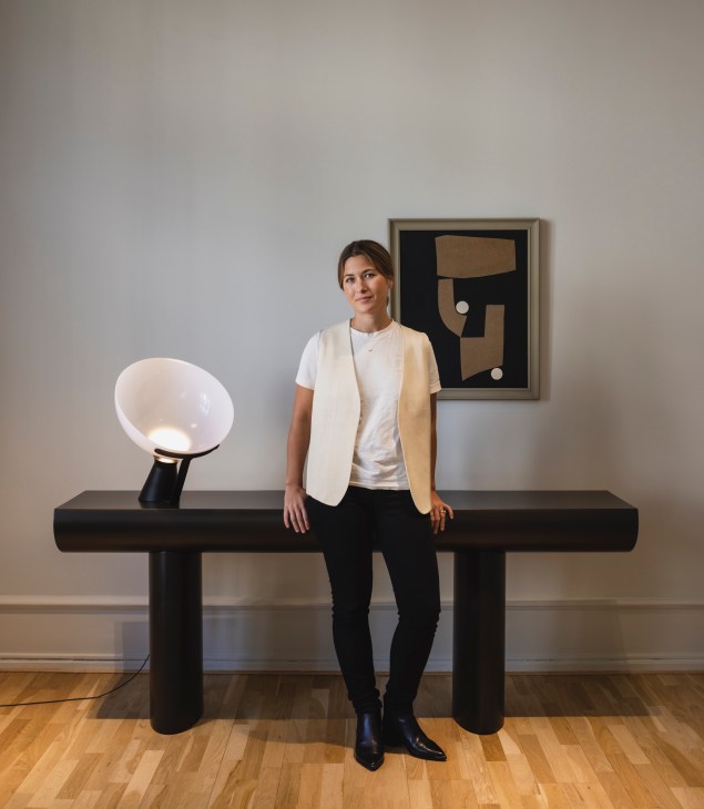 Sasha Bakholt from Karakter standing in a modern furniture showroom with wooden chairs and tables