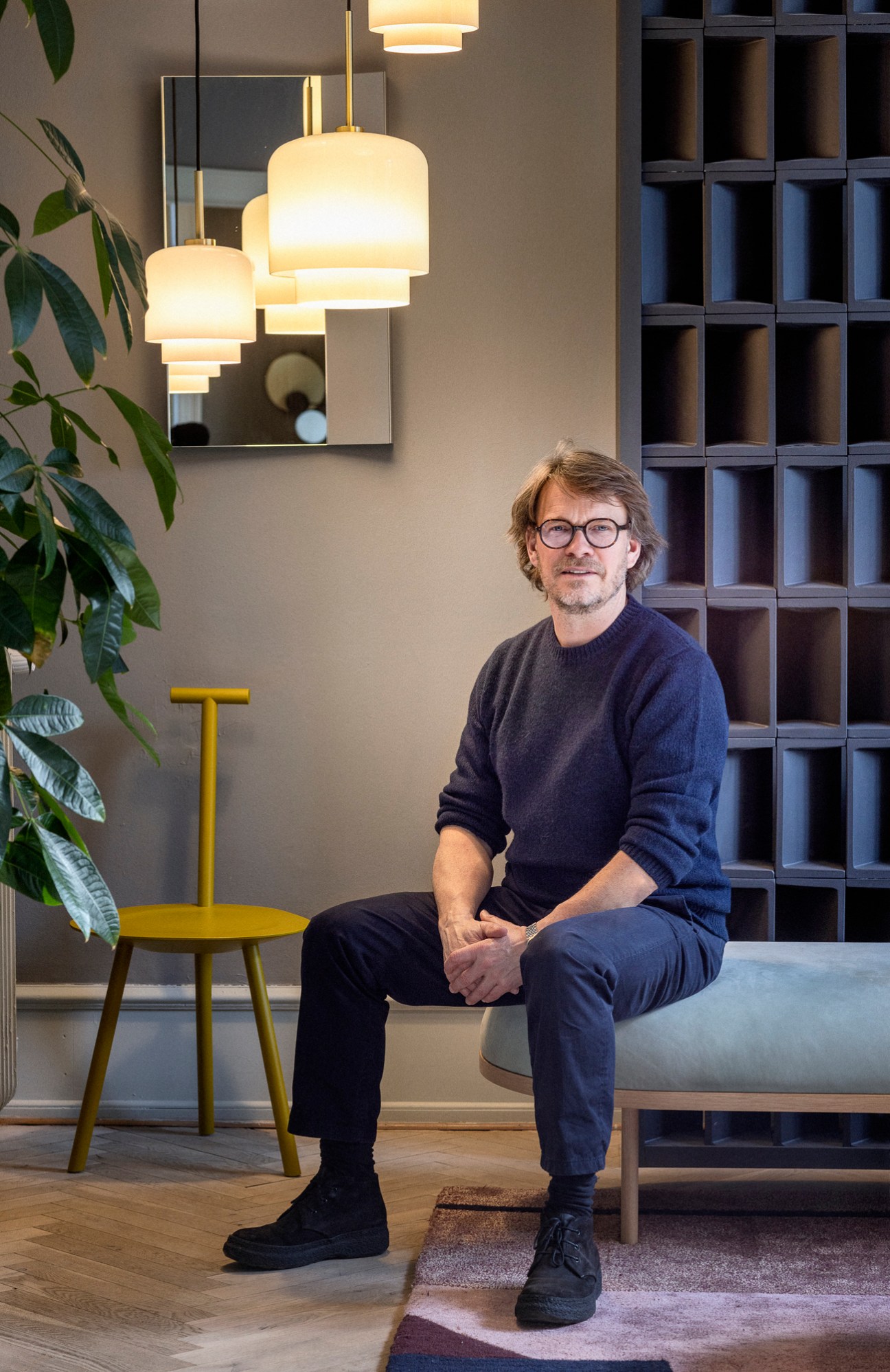 Thomas Ibsen sitting on a modern wooden chair in a showroom with pendant lights and shelving