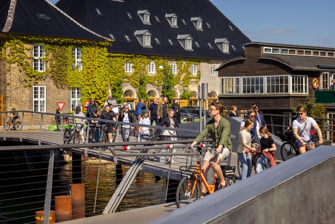Cyclists and pedestrians crossing a bridge over a canal in Amsterdam with ivy-covered historic buildings.