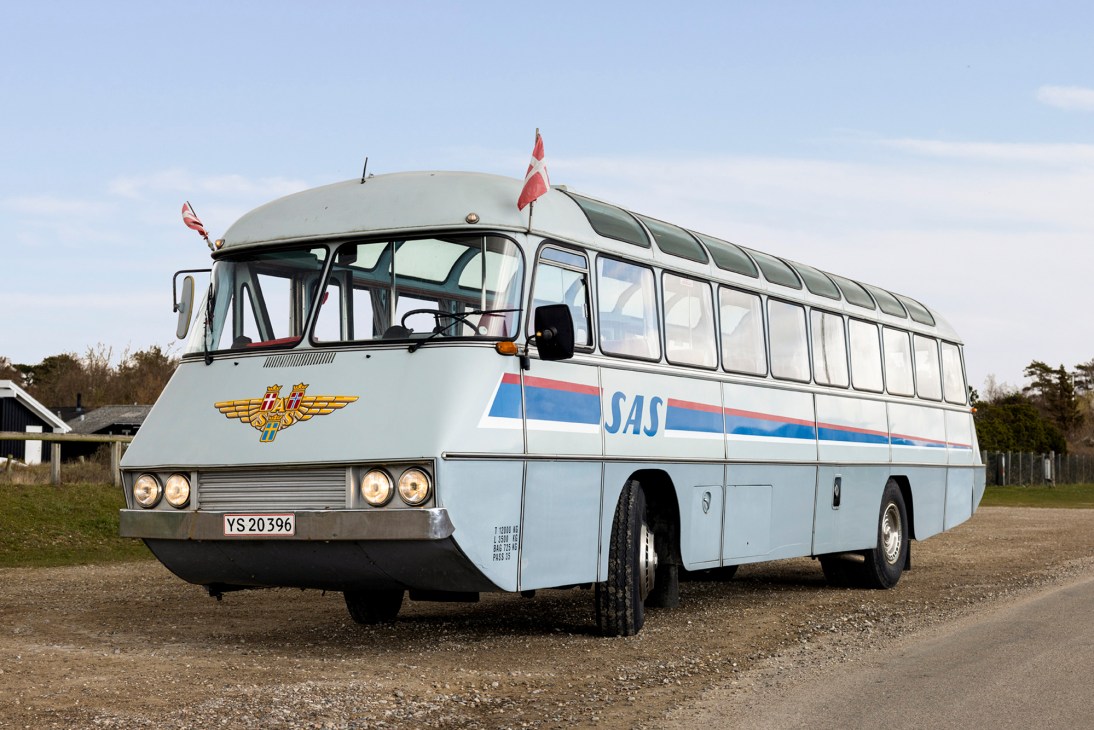 Vintage white and blue SAS bus with panoramic windows parked on gravel road in rural Danish countryside setting
