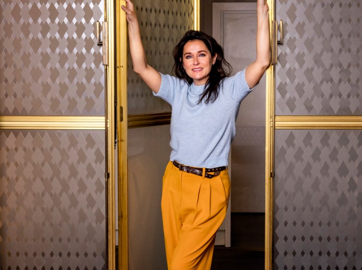 Sidse Babett Knudsen standing in doorway of ornate gold-framed glass doors with geometric patterned walls