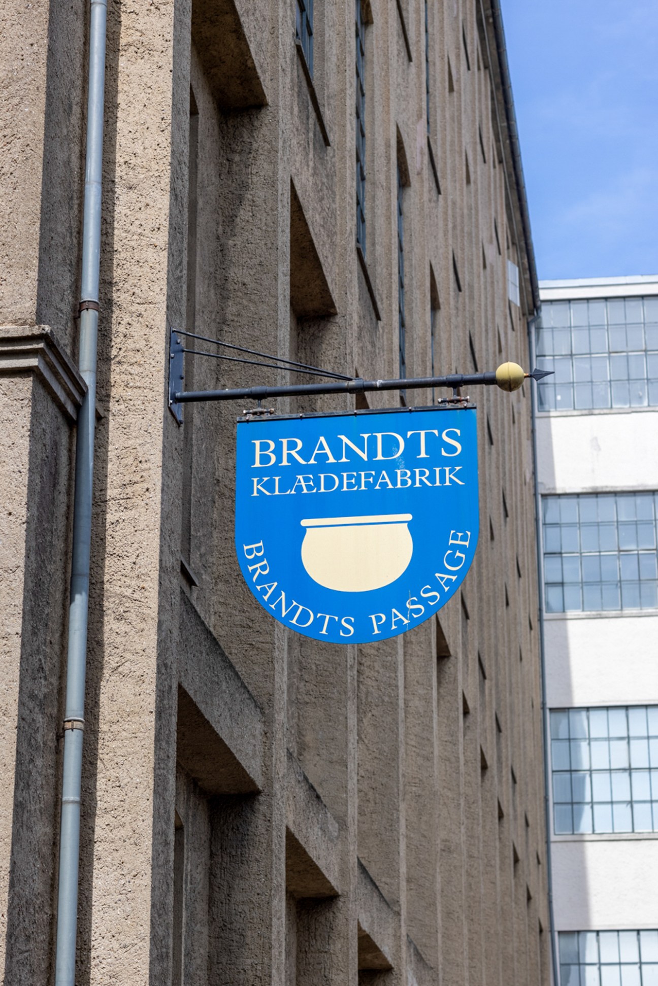 Blue circular sign for Brandts Klaedefabrik clothing factory mounted on concrete building wall in Odense
