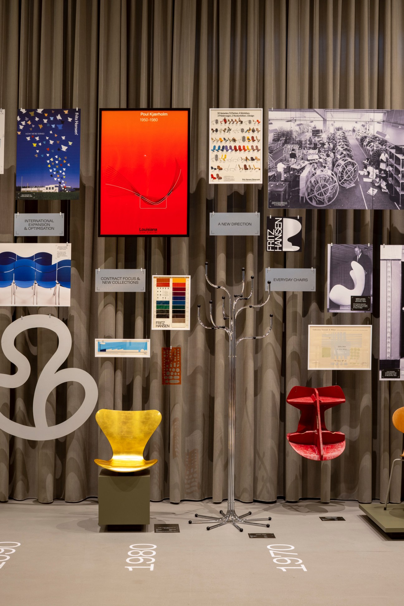 Museum display wall with Fritz Hansen furniture timeline, vintage posters, and chairs including yellow and red pieces